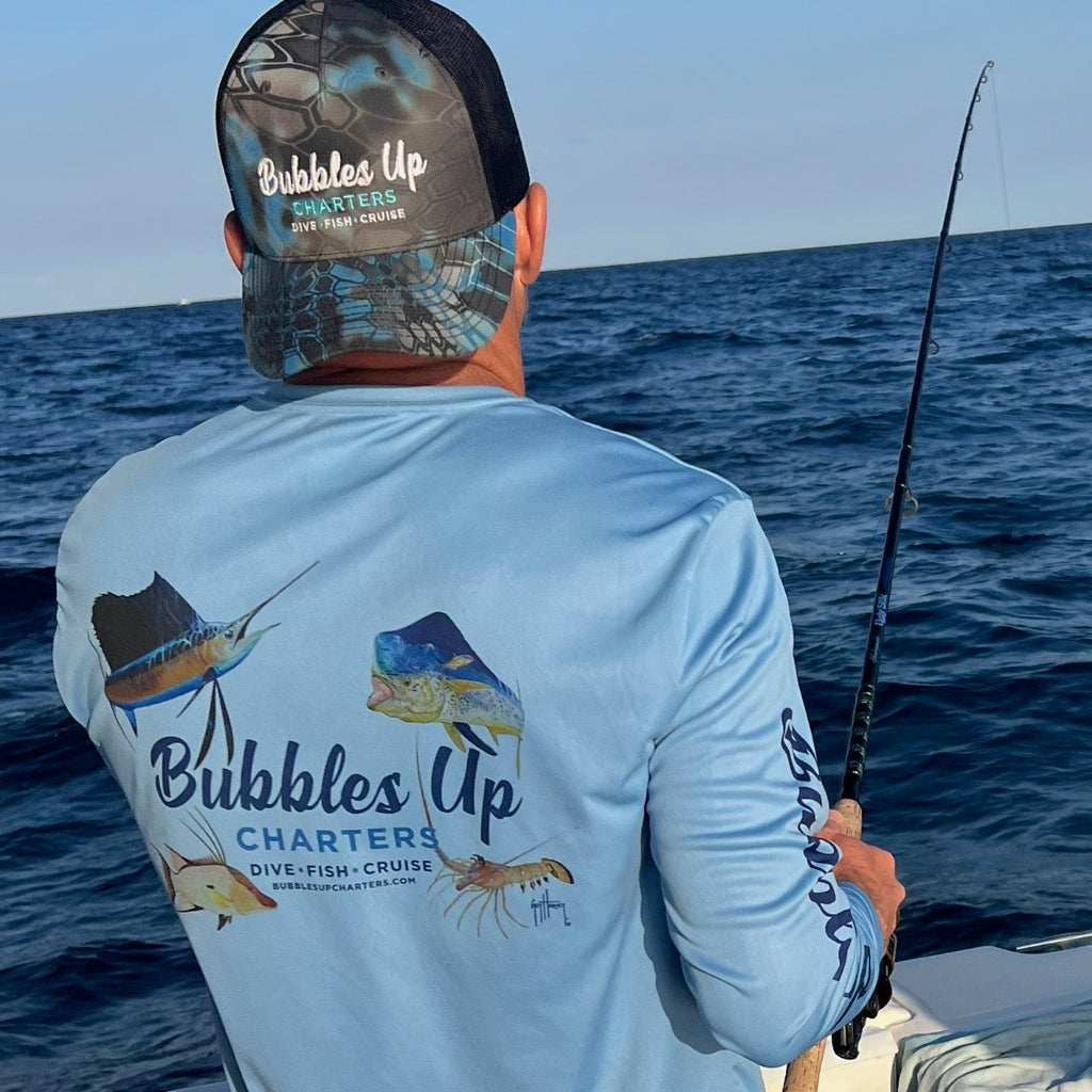 Man on a boat wearing a 'Bubbles Up Charters' shirt and cap, holding a fishing rod.